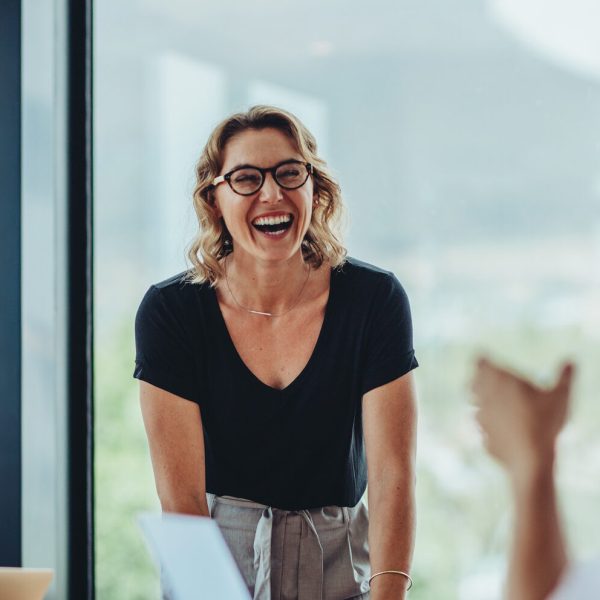 Businesswoman standing at conference table and laughing. Female professional smiling during a meeting in office boardroom.